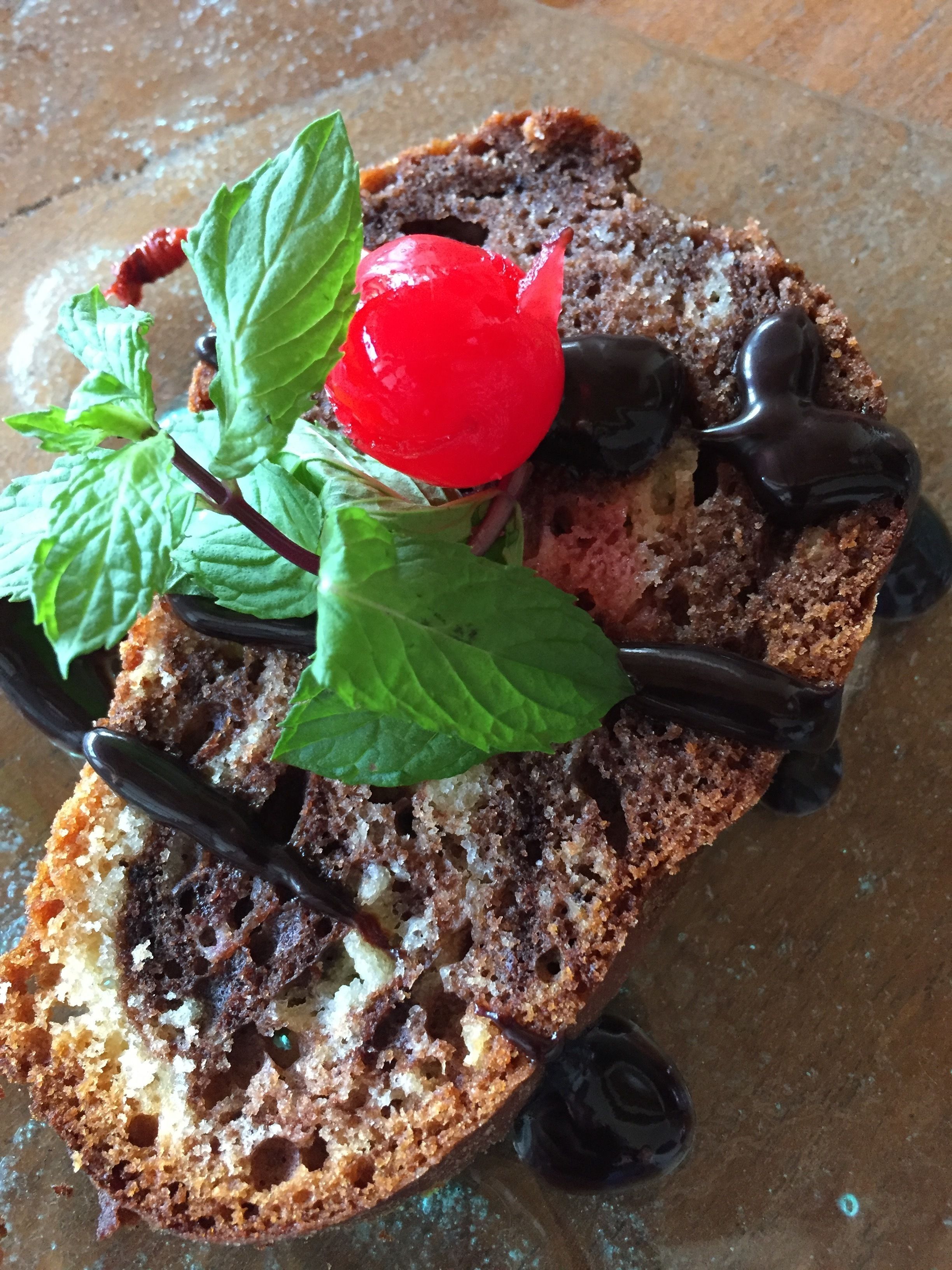 Una rebanada de pastel con chocolate y una cereza en la parte superior, decorada con hojas de menta.