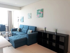 A modern living room with a blue sectional sofa, a glass coffee table, and a black console table with plants.