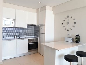 A modern kitchen with white cabinets, a black and white backsplash, a built-in microwave, a refrigerator, a stove, a toaster, and a wall clock.