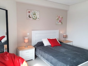 A bedroom with a bed, two bedside tables, a nightstand, a mirror, and two wall-mounted artworks.