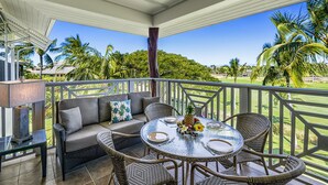 A covered outdoor seating area with wicker furniture, a glass table, and a view of a golf course.