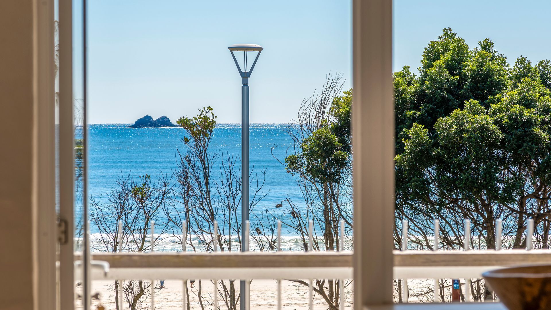 A beach view with a lamp post, trees, and a clear sky.
