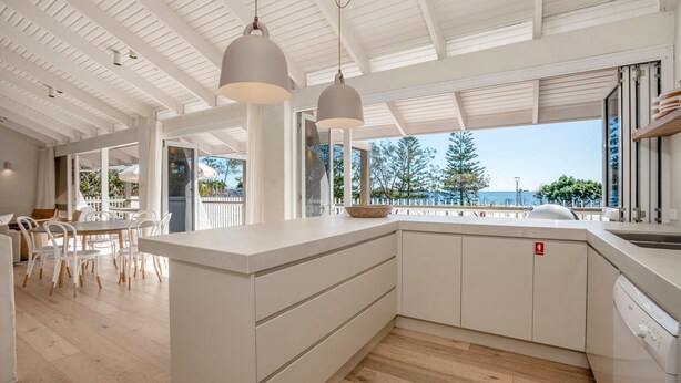 Eine moderne Küche mit einer großen Kochinsel, Pendelleuchten und Blick aufs Meer.