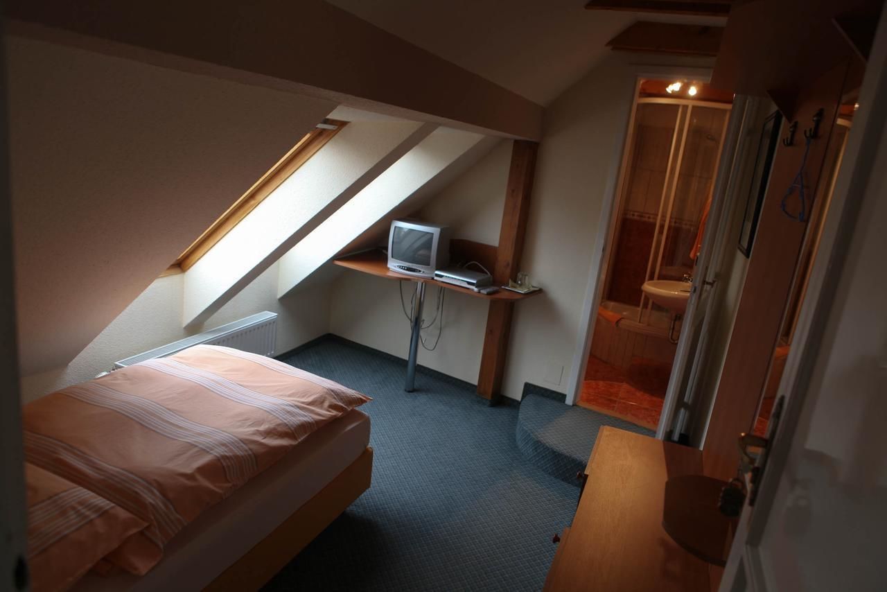 A compact bedroom with a single bed, a small desk with a computer, and a shower area.