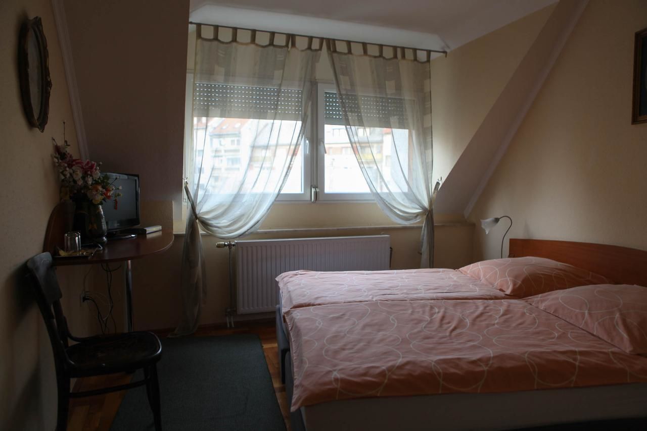A bedroom with a bed, a desk with a computer, a chair, and a window with curtains.