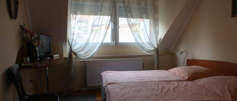 A bedroom with a bed, a desk with a computer, a chair, and a window with curtains.