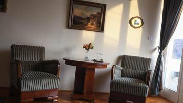 Una habitación con dos sillones tapizados, una mesa de madera con un florero y un cuadro en la pared, además de una ventana con cortinas.