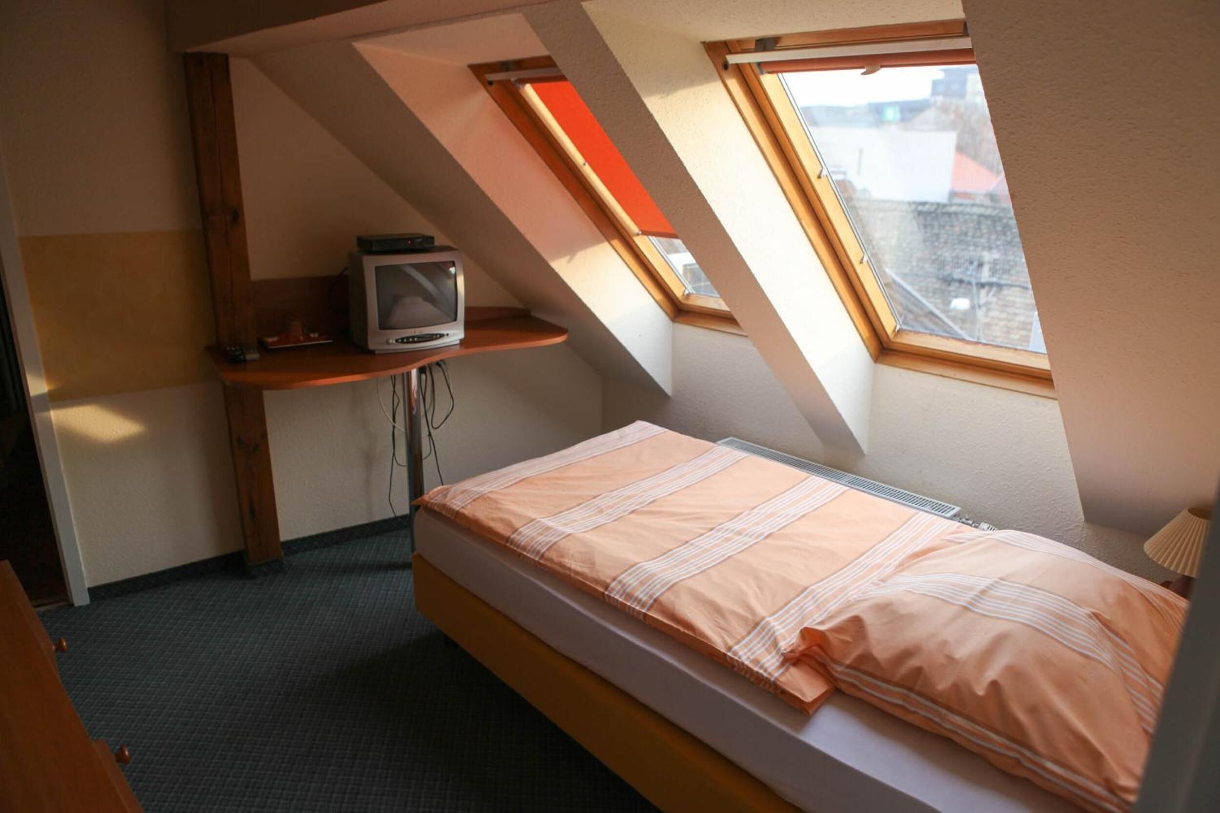 A small, sloped room with a bed, a TV on a shelf, and a window.