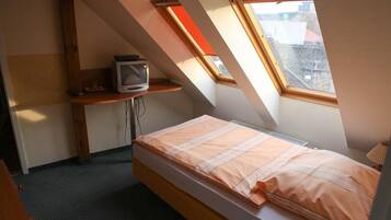 A small, sloped room with a bed, a TV on a shelf, and a window.