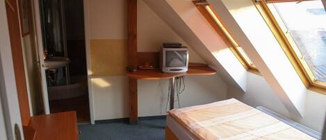 A small, compact room with a bed, a desk with a television, and a window.