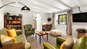 A cozy living room with green sofas, a bookshelf, a coffee table, and a large window with curtains. - Wanaka Stone Cottage - Wanaka Holiday Home (Wanaka)