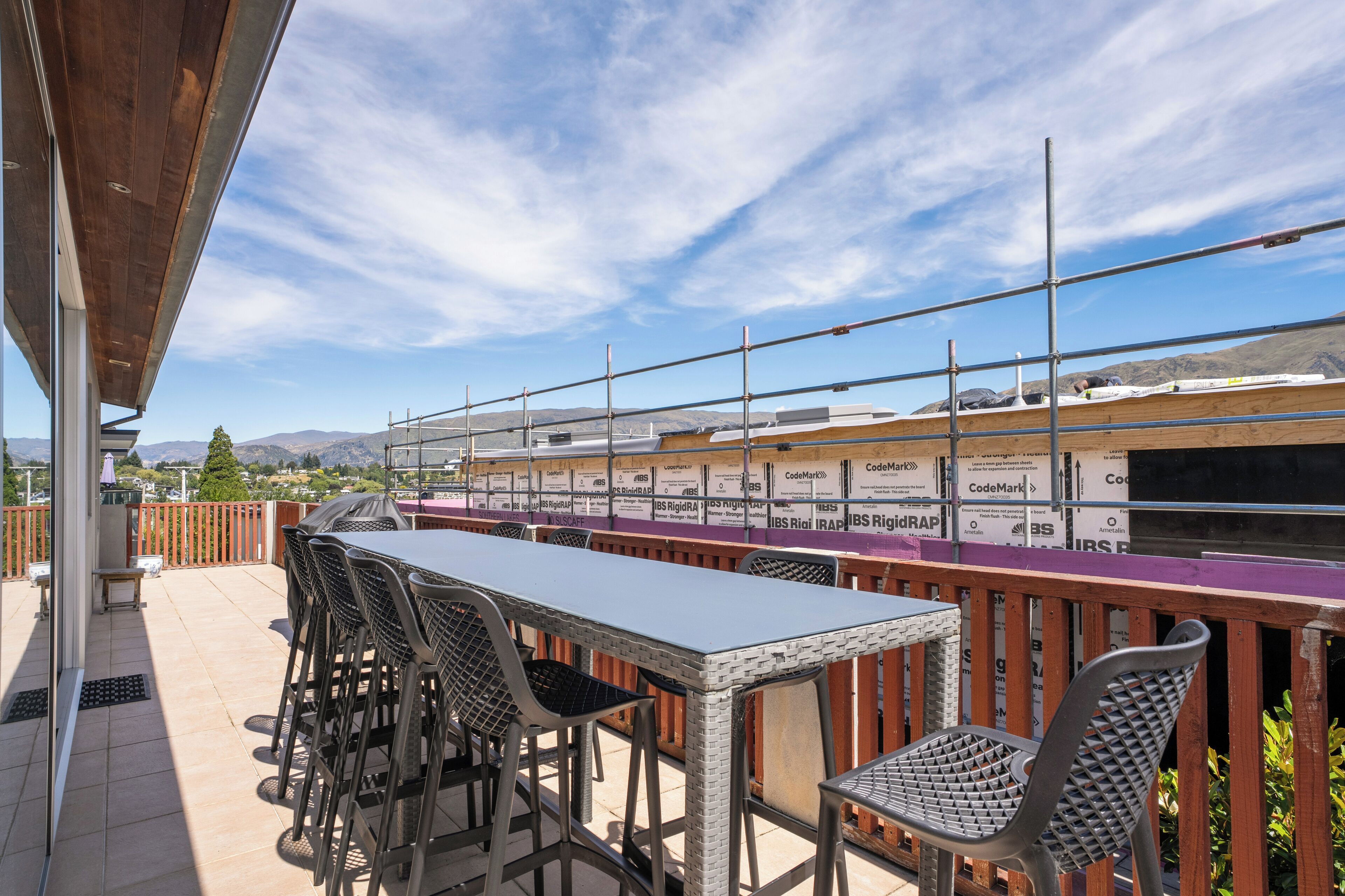 An outdoor patio with a long table and chairs, a wooden fence, and a view of distant mountains.