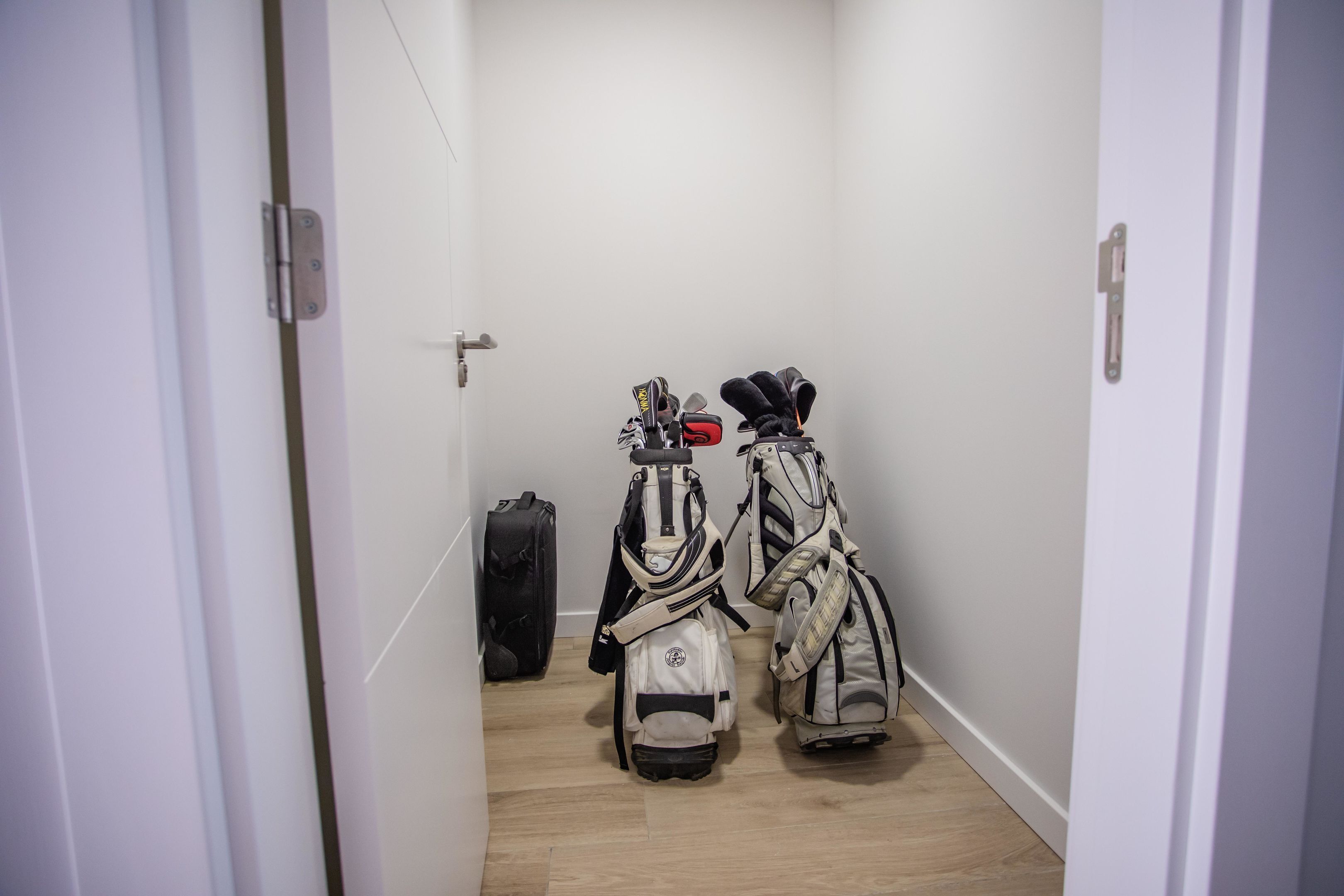 A narrow hallway with two golf bags and a suitcase against the wall.