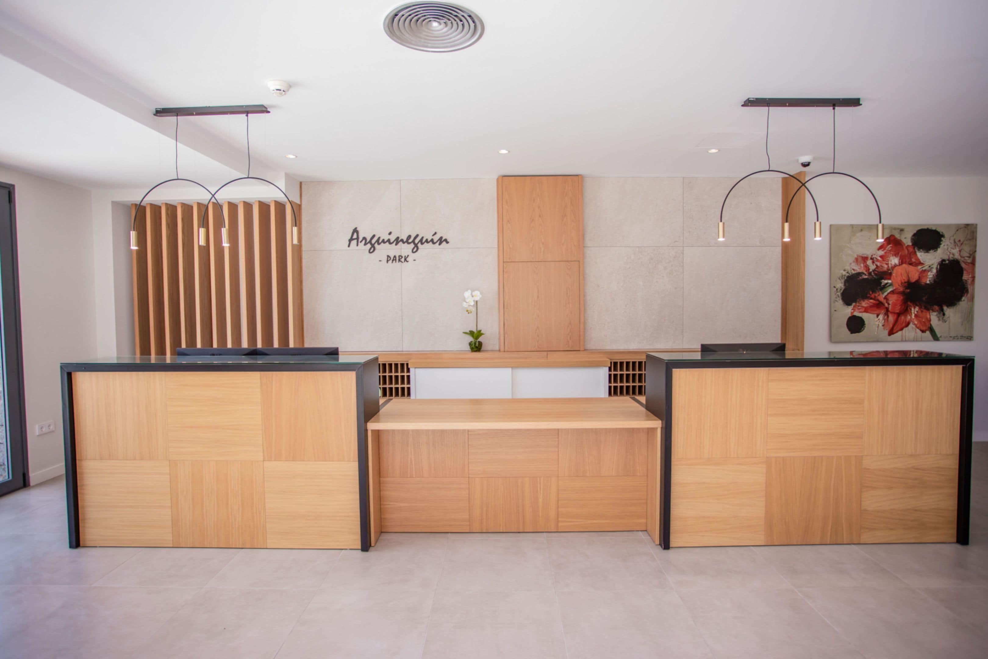 A reception desk with a wooden finish, a wall-mounted sign reading "Argünesfúin - DARK", and a large floral painting on the right.