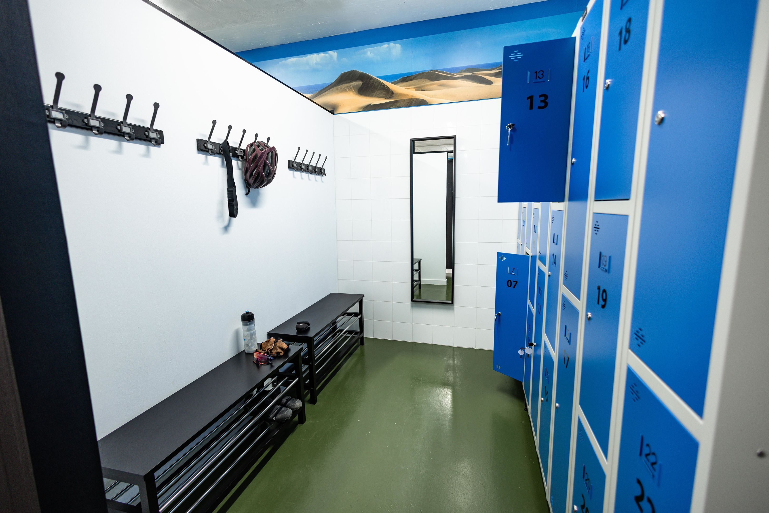 A locker room with numbered lockers, a bench, and a mirror.