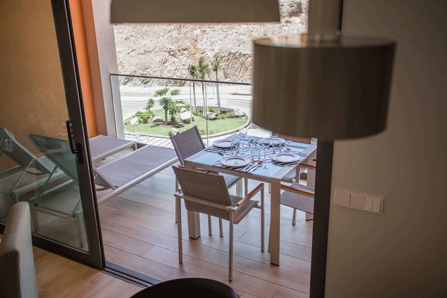 A dining area with a table set for four, a laptop on the table, and a view of a landscaped garden through a glass door.