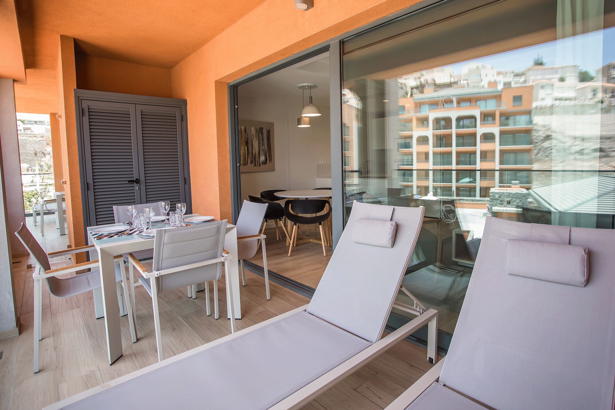 En balkon med spiseplads, liggestole og udsigt til bygninger.