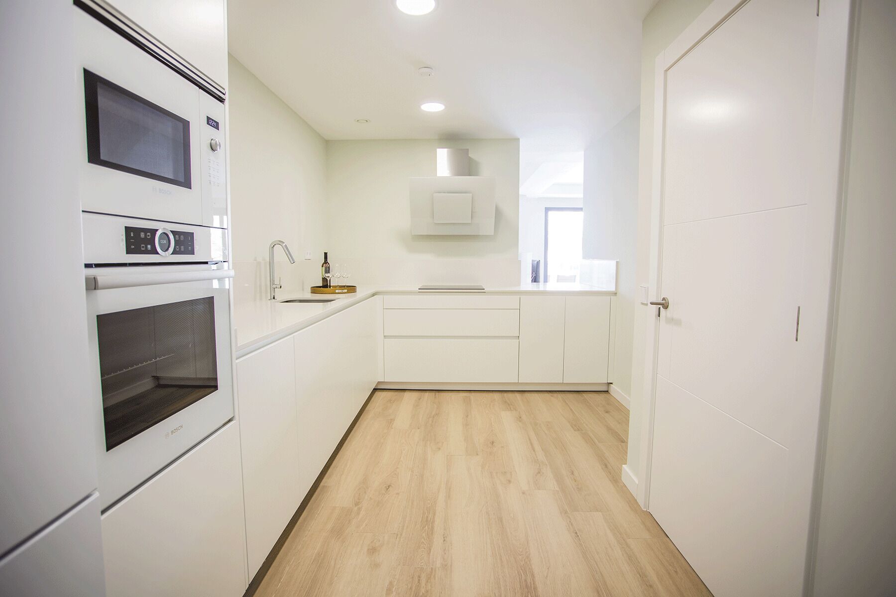 A modern kitchen with white cabinetry, a Bosch oven, and a microwave.