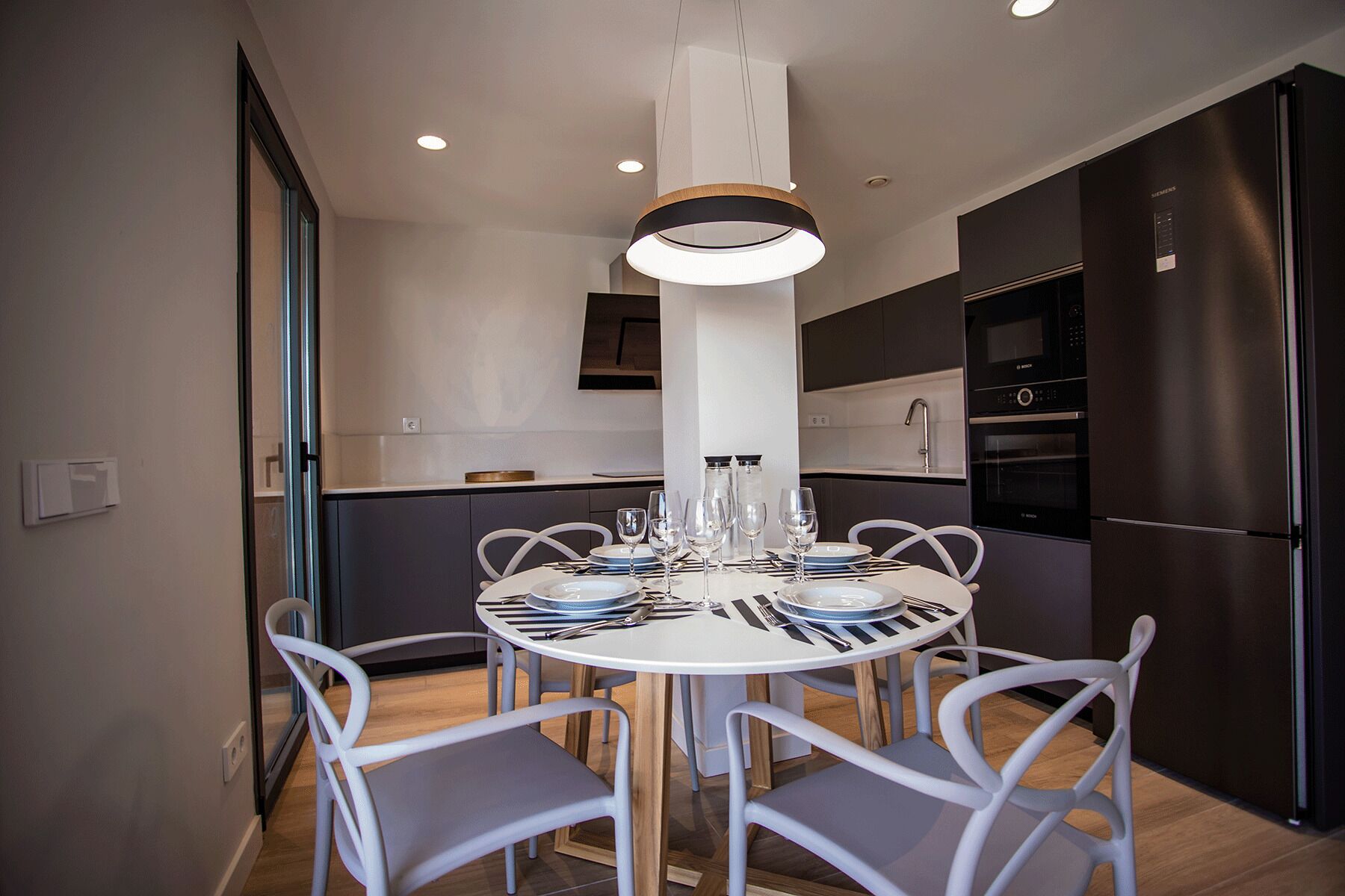 Una cocina moderna con una mesa de comedor redonda, sillas blancas y electrodomésticos de acero inoxidable.