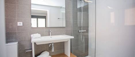 Une salle de bain moderne avec une douche à parois de verre, un lavabo blanc et une étagère en bois où sont posées des serviettes.