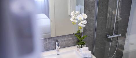 Un baño moderno con un lavamanos blanco, un espejo y una zona de ducha.