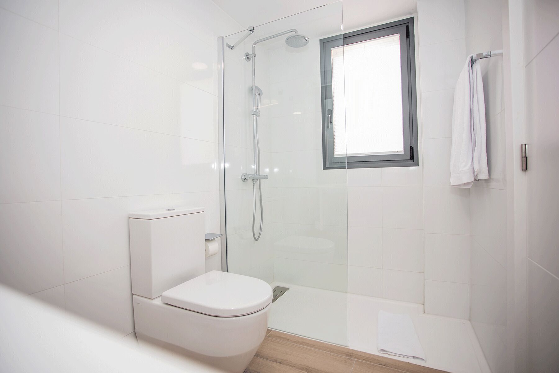 A modern bathroom with a glass-enclosed shower, a toilet, and a window.