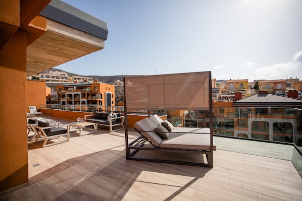 Relax on a rooftop with a comfortable bed, lounge chairs, and a small table under a shaded canopy.