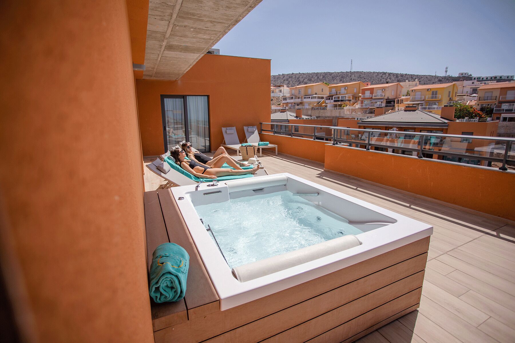 A rooftop terrace with a hot tub, lounge chairs, and a view of surrounding buildings.