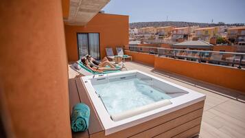 A rooftop terrace with a hot tub, lounge chairs, and a view of surrounding buildings.