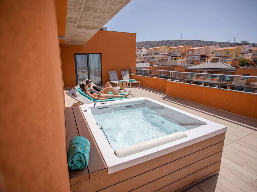 A rooftop terrace with a hot tub, lounge chairs, and a view of surrounding buildings.