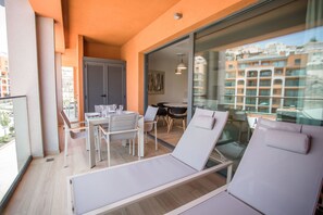 A balcony with a dining area, two lounge chairs, and a glass door leading to a city view. - Arguineguin Park By Servatur VV (Mogan)