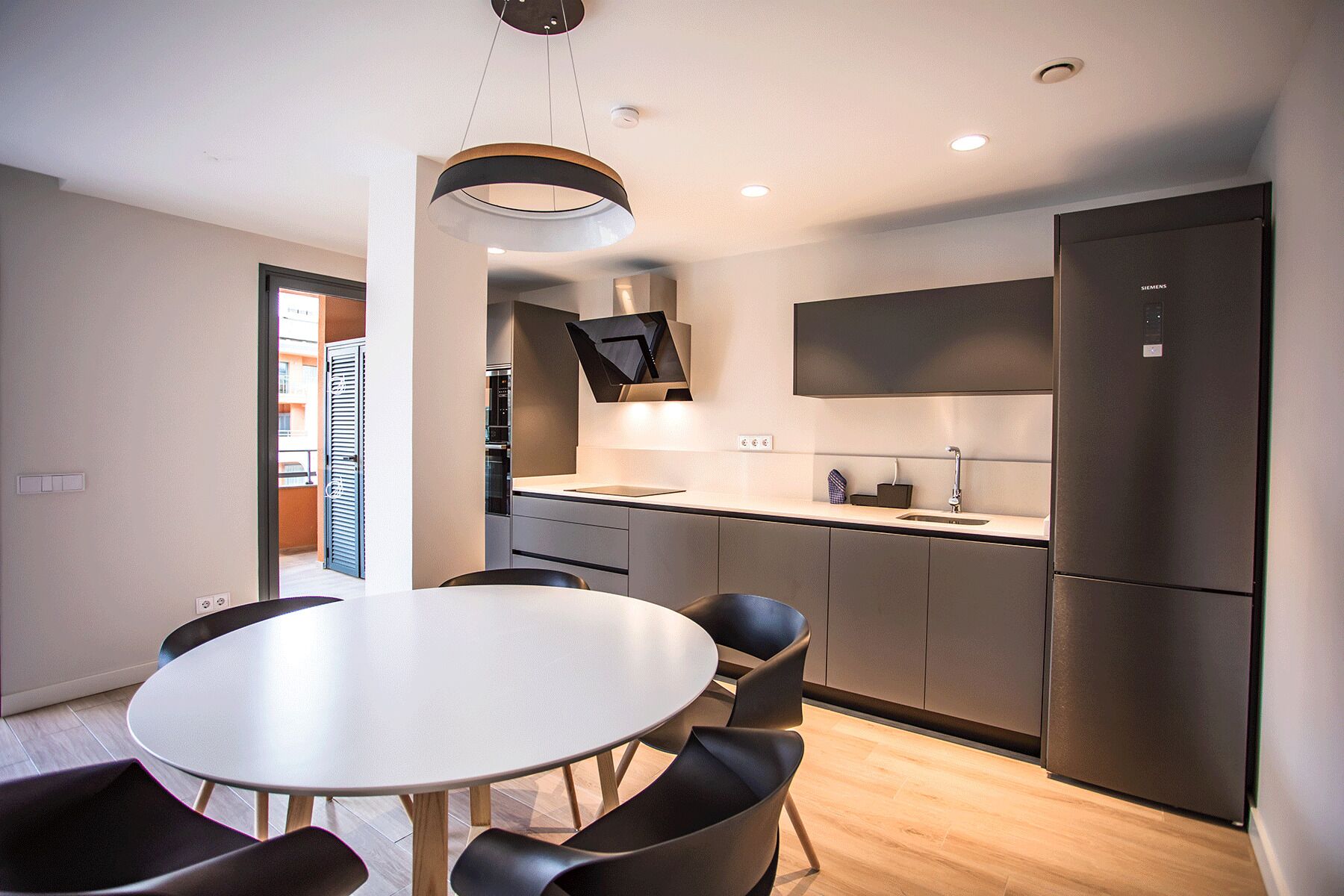 Una cocina moderna con horno empotrado, un lavamanos y un refrigerador. Hay un comedor con una mesa redonda y sillas.
