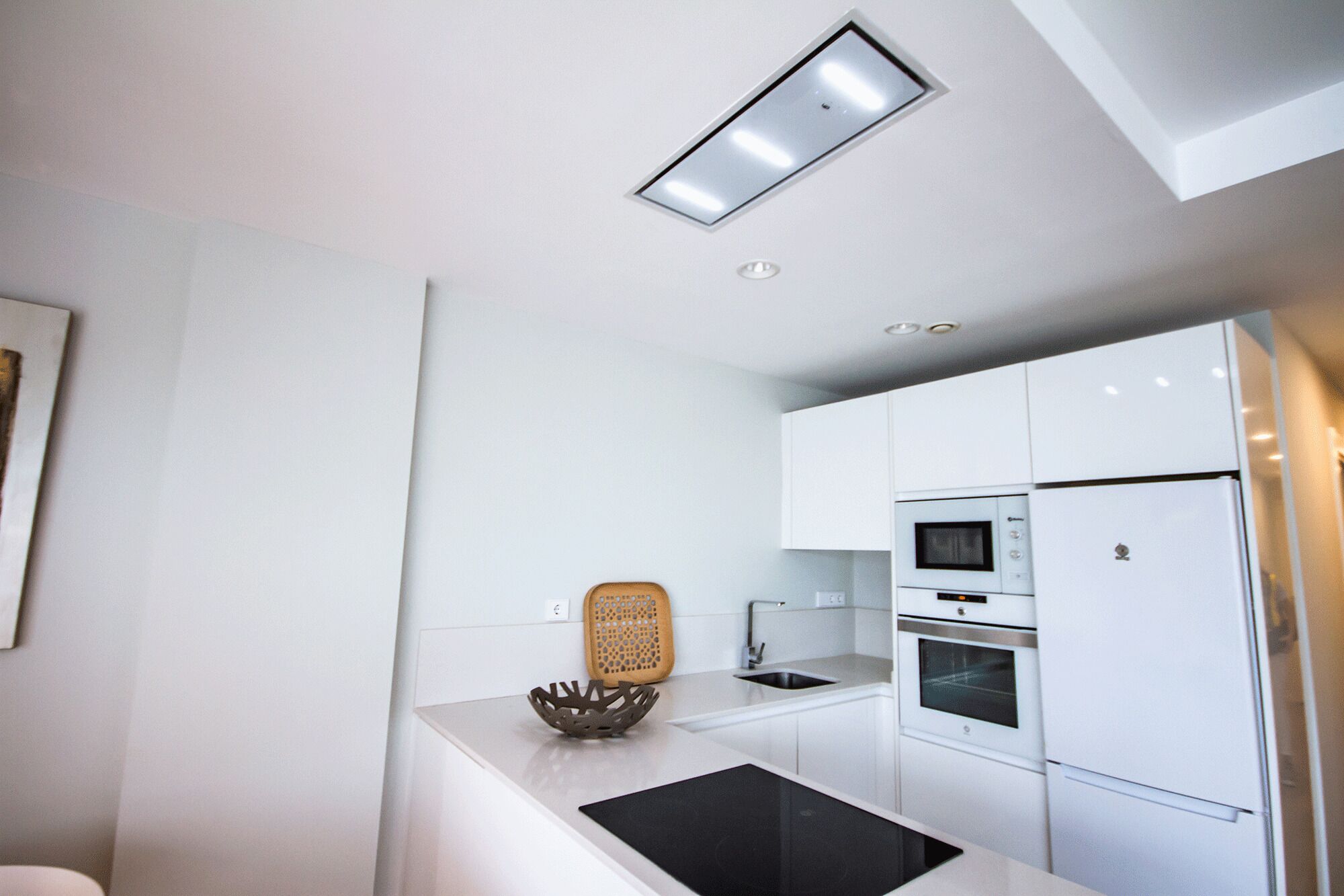 A modern kitchen with white cabinets, a built-in oven, a microwave, and a refrigerator.