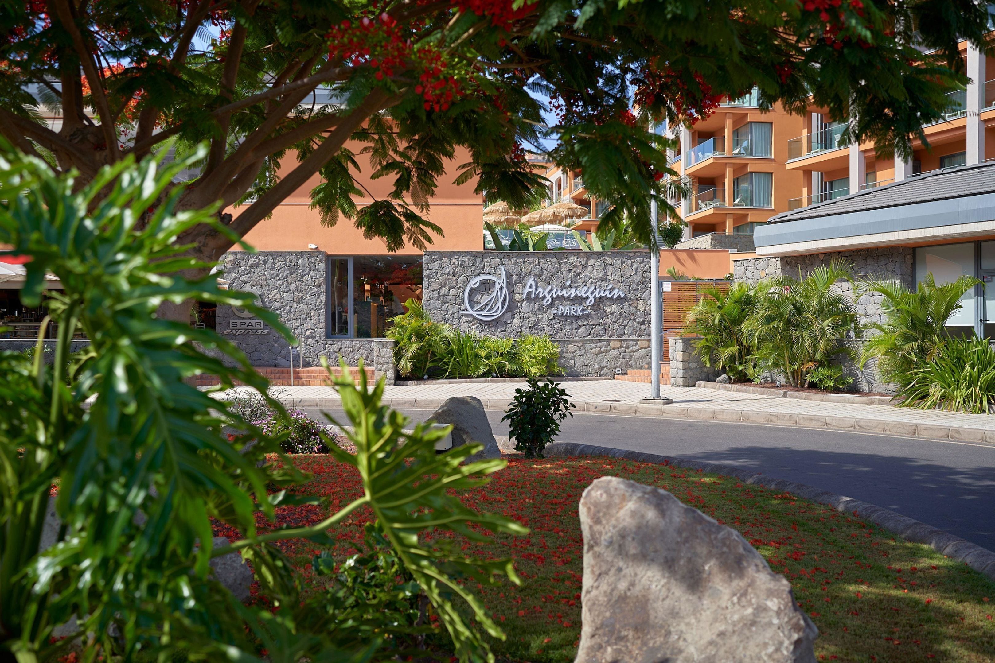 Ein Hotel mit steinverkleidetem Eingang, einer Beschilderung und einem angelegten Bereich mit roten Blumen und Grünpflanzen.