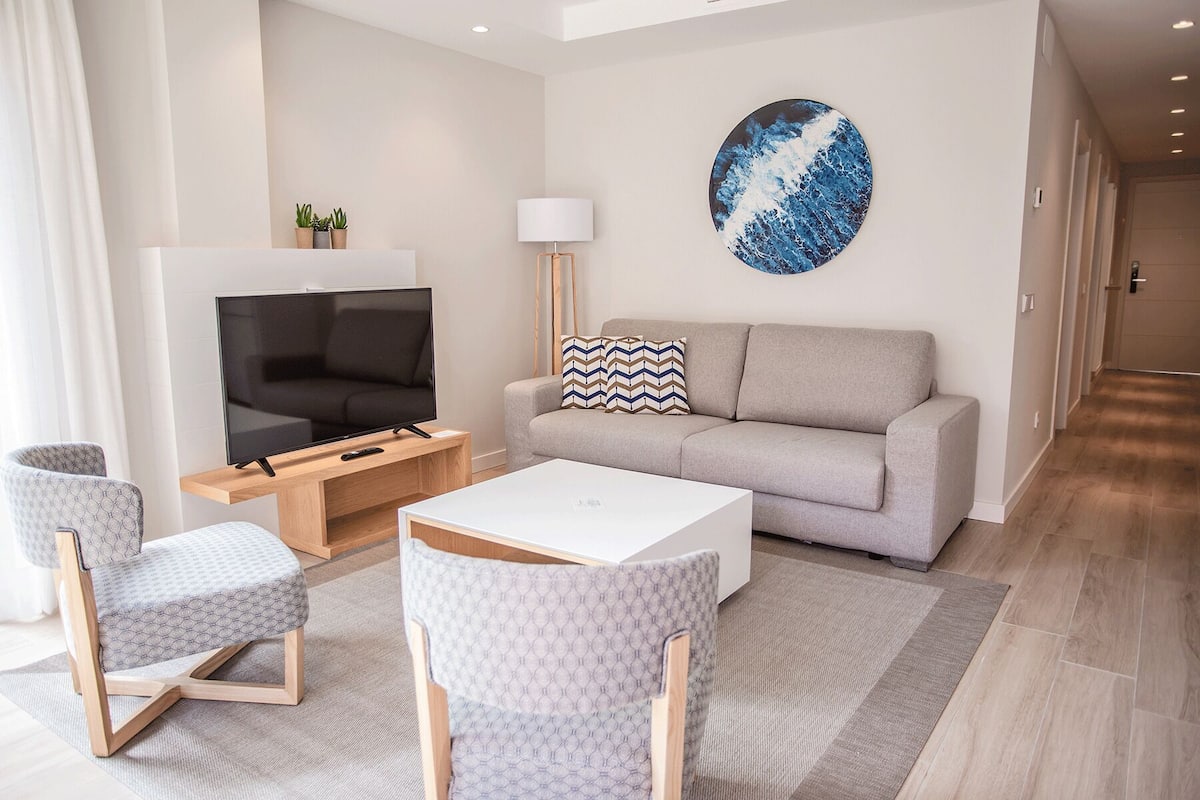 Una sala de estar moderna con un televisor de pantalla plana, sofá gris, sillas estampadas y una obra de arte circular en la pared.