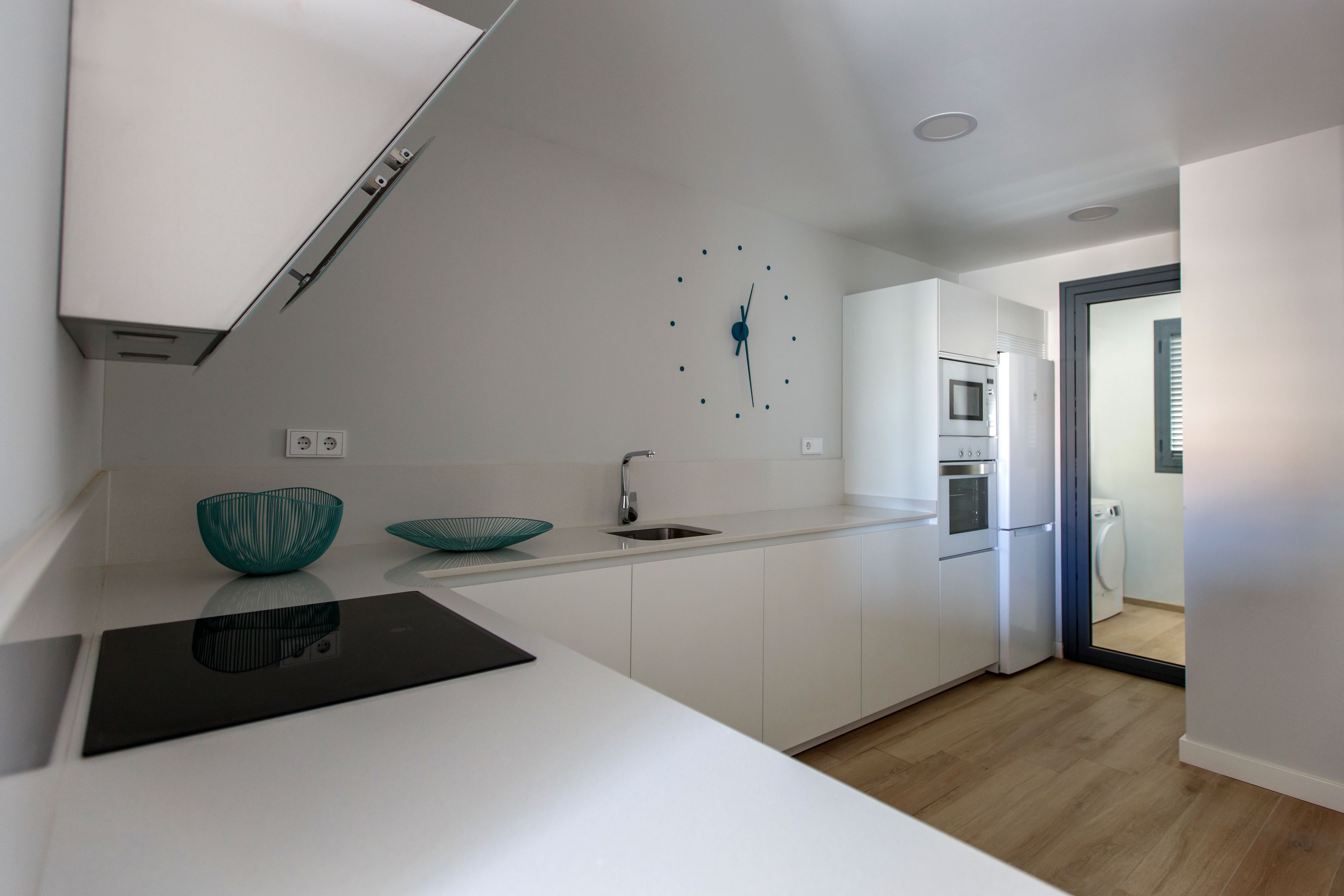 Une cuisine moderne avec des meubles blancs, une plaque de cuisson à induction noire et un saladier turquoise posé sur le plan de travail.