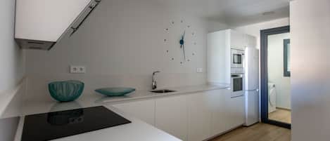 Une cuisine moderne avec des meubles blancs, une plaque de cuisson à induction noire et un saladier turquoise posé sur le plan de travail.