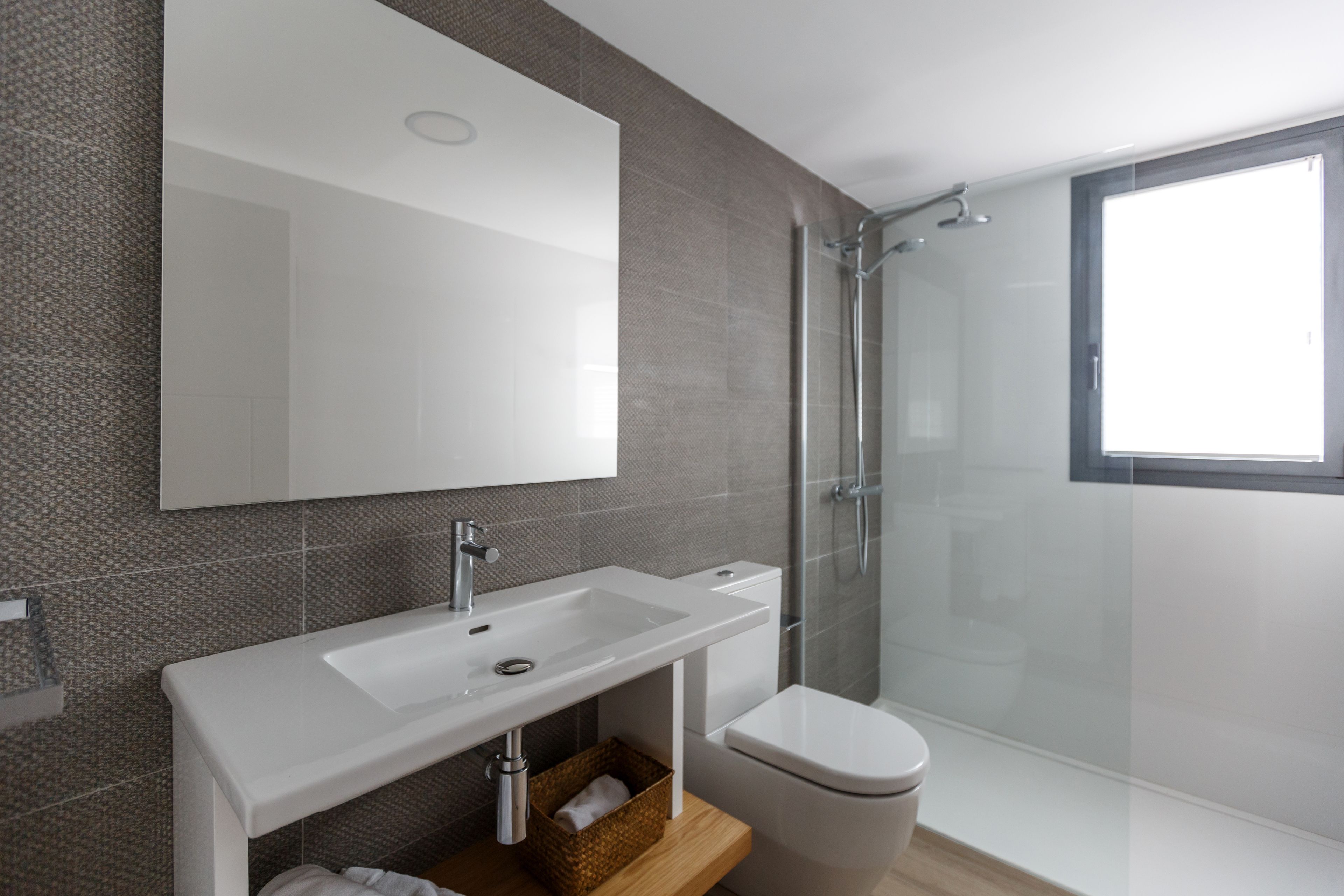 Un baño moderno con lavamanos, espejo y inodoro blancos.