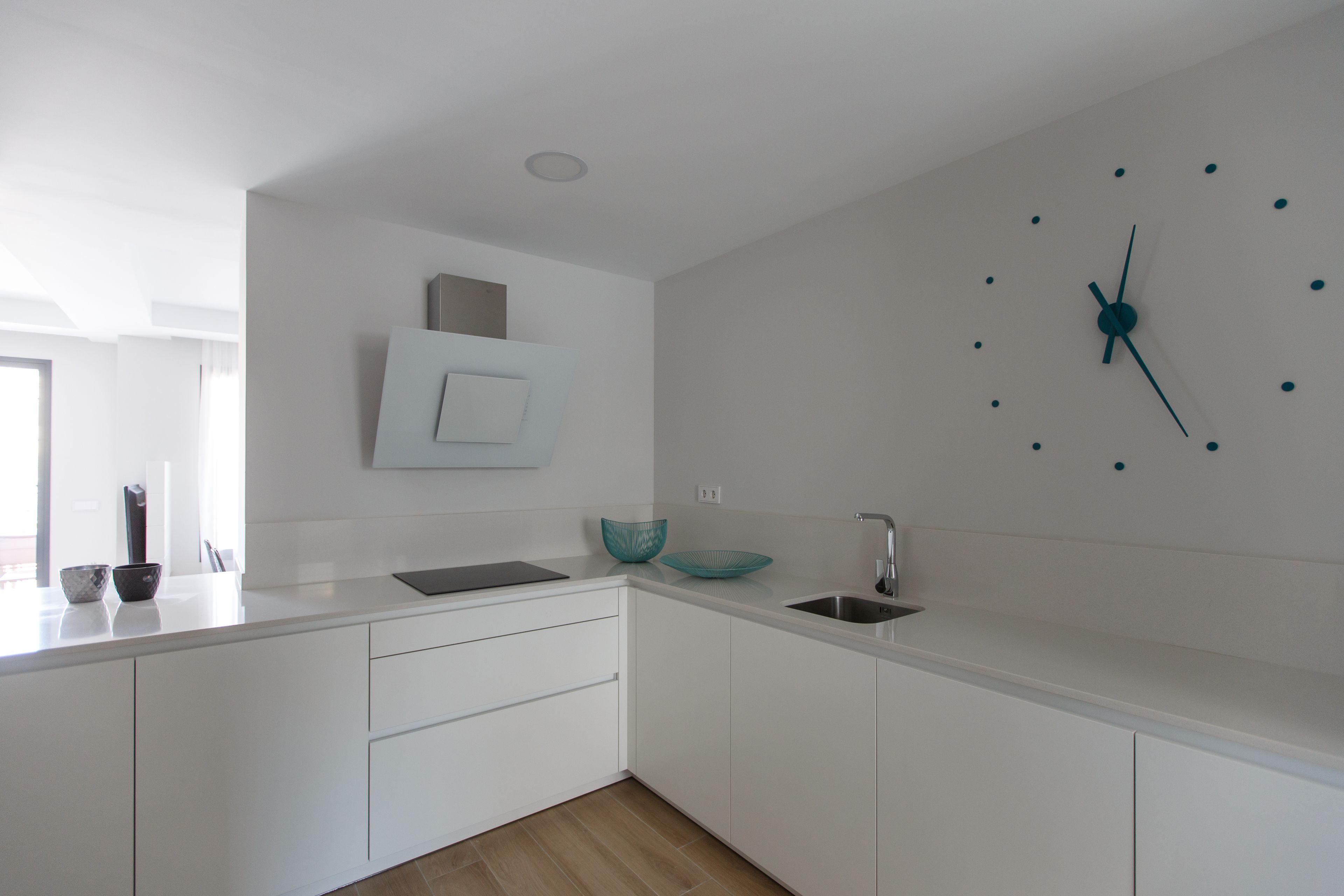 A modern kitchen with white cabinetry, a built-in sink, and a wall-mounted clock.