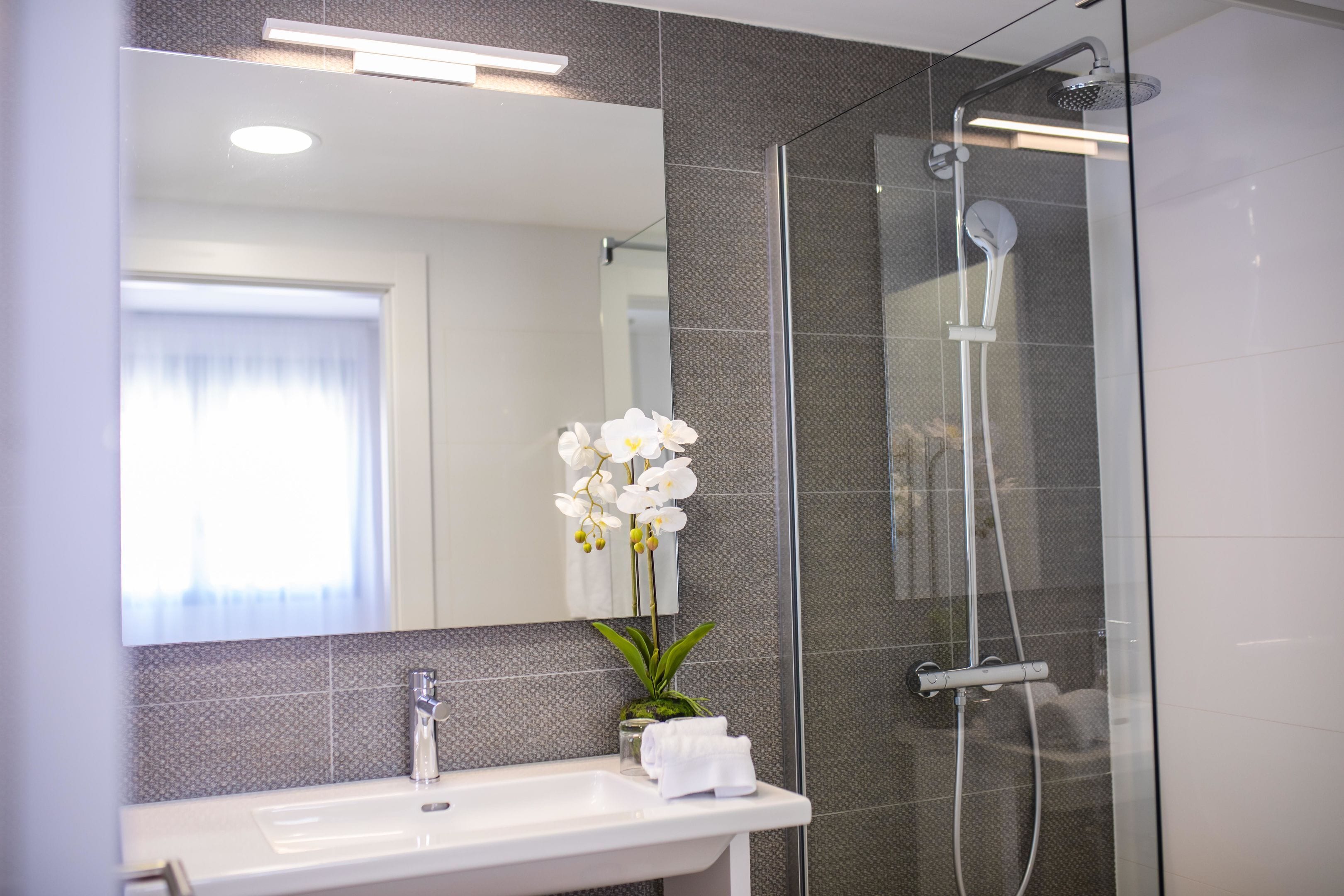 Ein modernes Badezimmer mit Duschkabine aus Glas, einem weißen Waschbecken und einem Spiegel darüber.