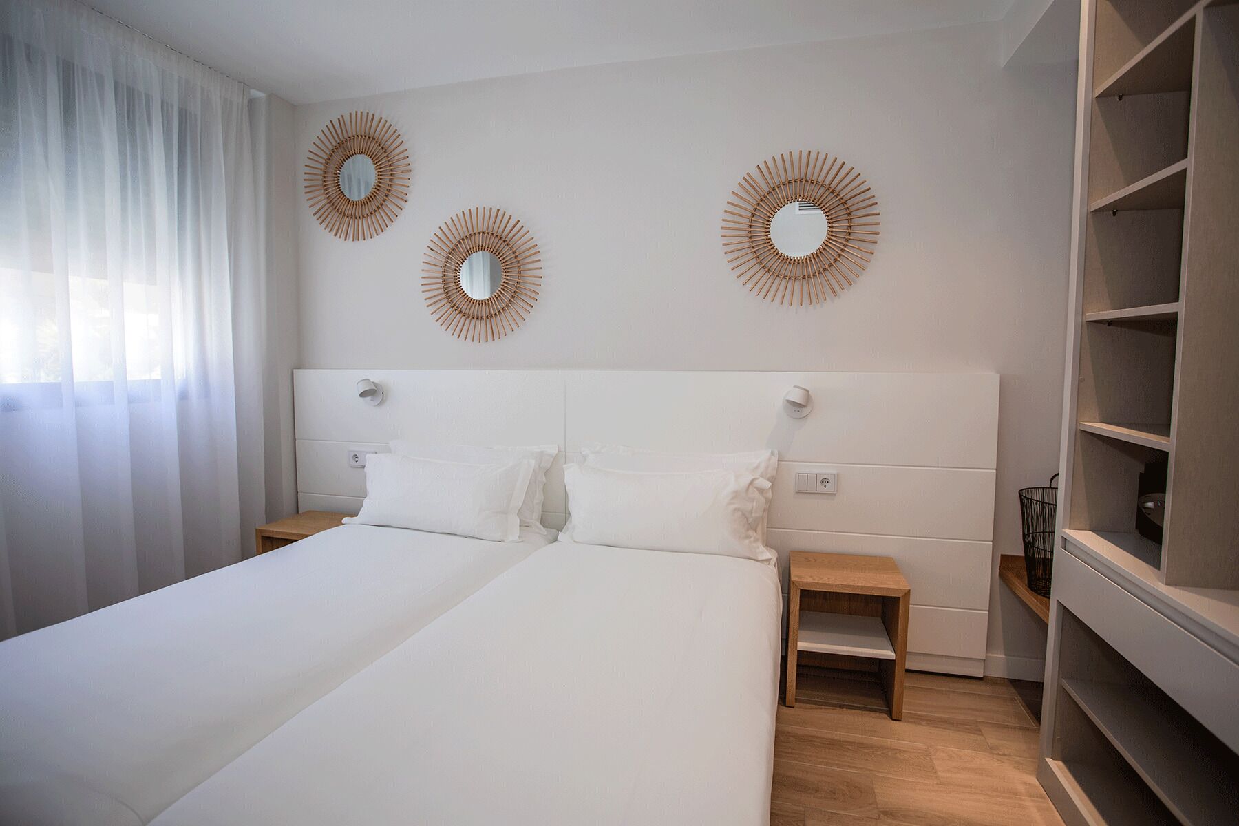 A modern bedroom with a large bed, two bedside tables, a wardrobe, and three wall-mounted mirrors.