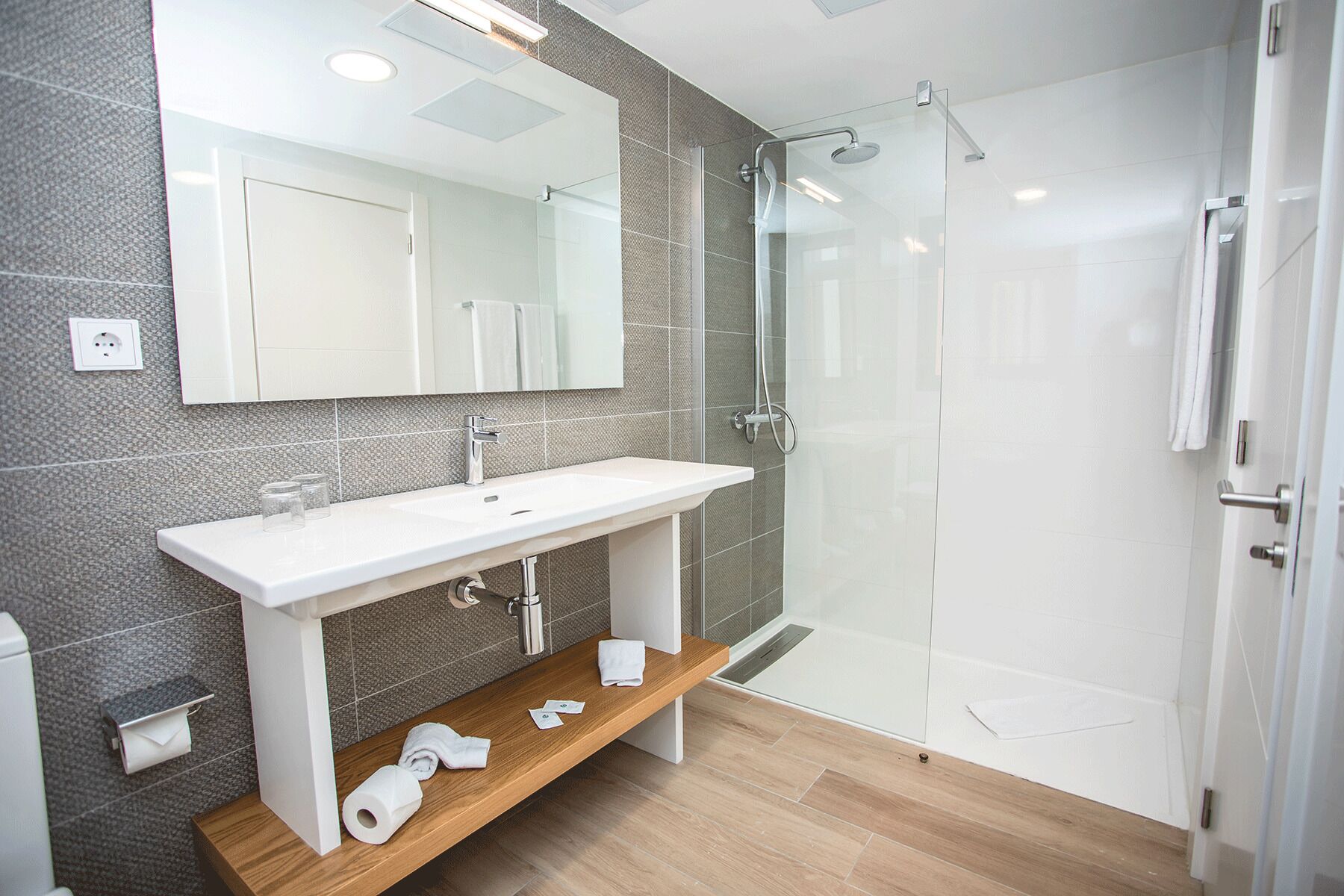 Un baño moderno con lavamanos blanco, espejo y cabina de ducha de vidrio.