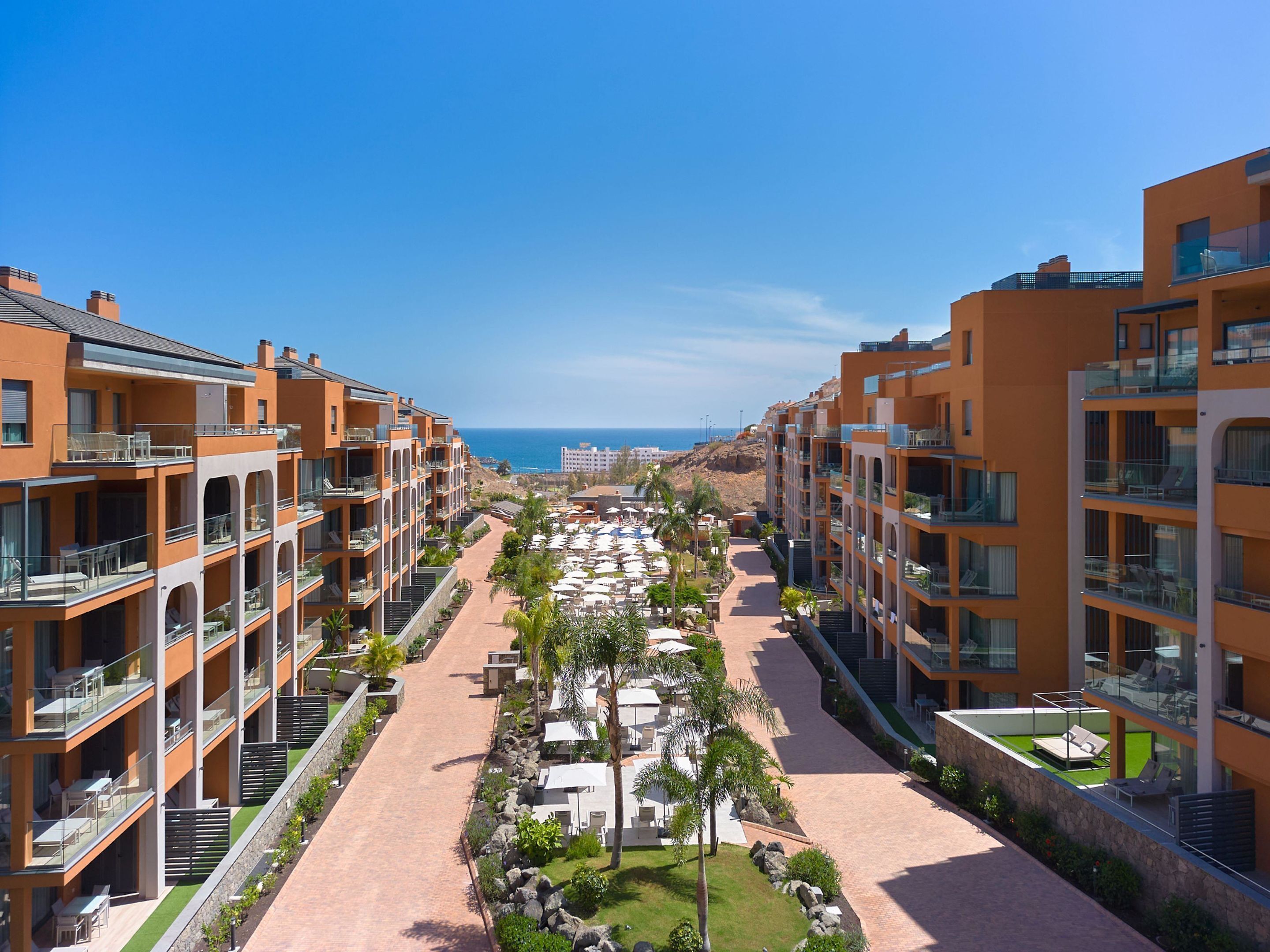A resort with multiple-story buildings, outdoor seating areas, and a view of the ocean.