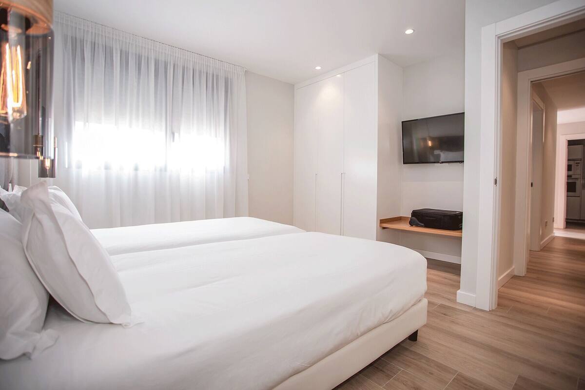 Una habitación de hotel moderna con una cama grande, un televisor de pantalla plana montado en la pared y suelo de madera.