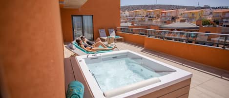 Une terrasse sur le toit avec un jacuzzi, des chaises longues et une vue sur la ville.