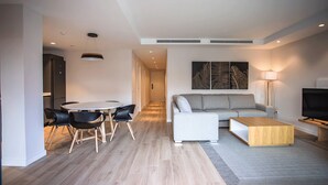 A modern living room with a grey sofa, a coffee table, and a dining area with a round table and chairs.