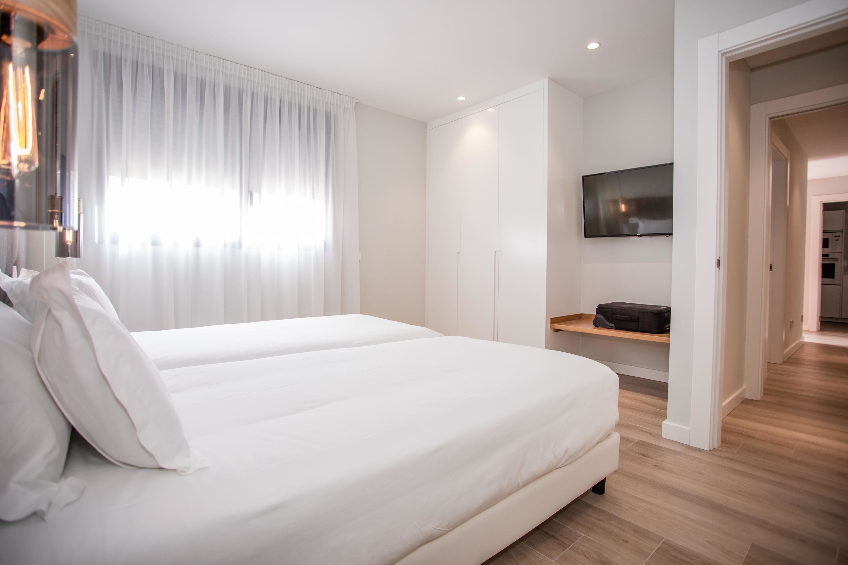 Una habitación de hotel moderna con una cama grande, un televisor de pantalla plana en la pared y piso de madera.