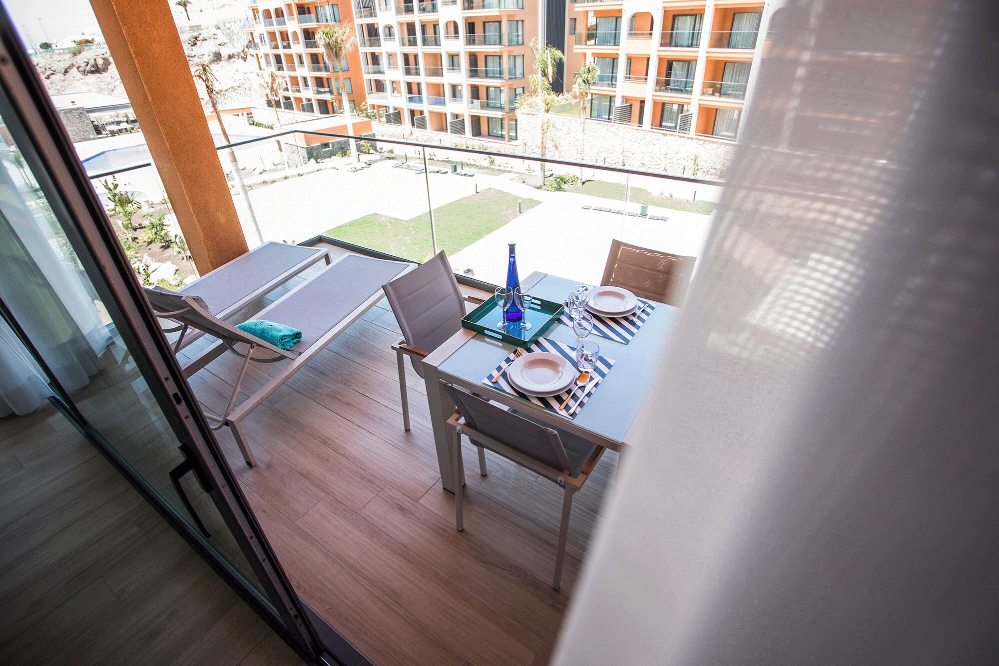 Uma varanda com uma mesa de jantar posta para dois, com vista para um pátio e edifícios ao fundo.