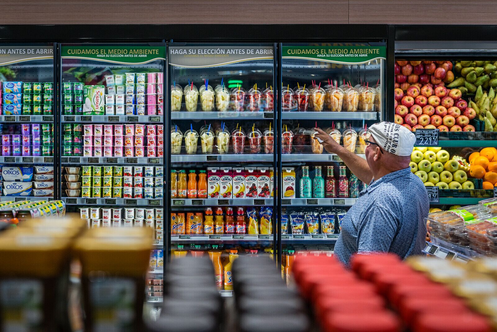 Una tienda de comestibles con dispensadores refrigerados para bebidas, estantes llenos de diversas opciones y una sección de productos frescos.