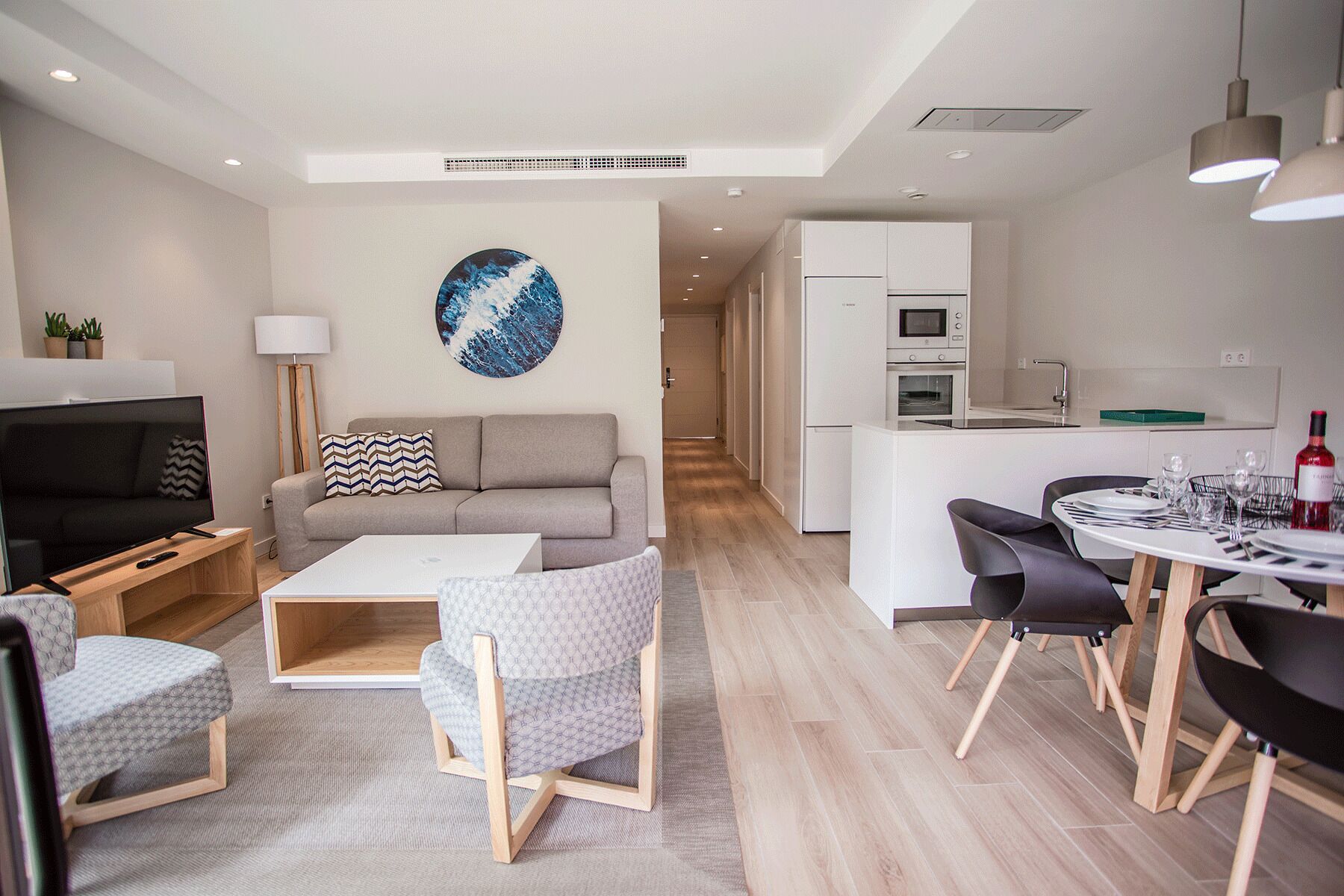 A modern living room with a sofa, coffee table, and chairs, a dining area with a table and chairs, and a kitchen with appliances.
